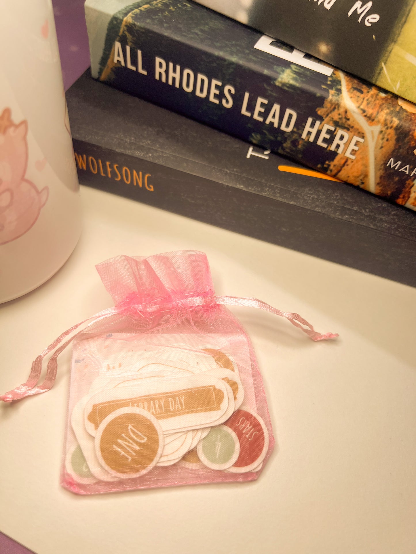 Pink drawstring bag with stickers on a surface with books in the background