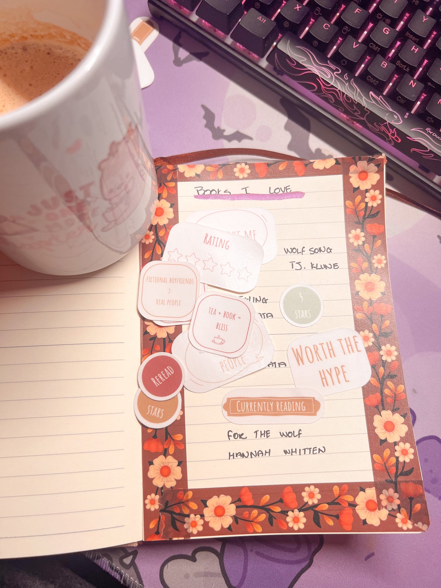 Notebook with a decorative cover featuring text and floral designs, next to a cup of coffee and a keyboard.