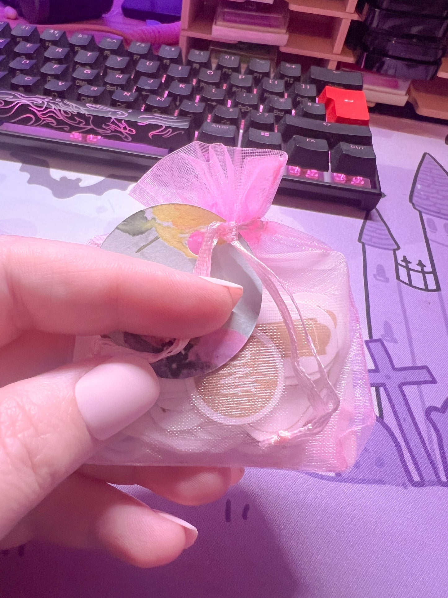 Hand holding a pink drawstring bag with stickers with a keyboard in the background.